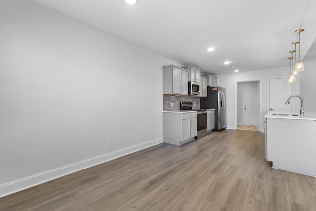 kitchen featuring decorative light fixtures, light hardwood / wood-style floors, tasteful backsplash, appliances with stainless steel finishes, and sink