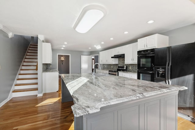 kitchen featuring black appliances, white cabinets, sink, light stone countertops, and a large island