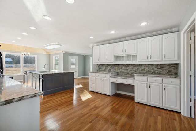 kitchen featuring hanging light fixtures, dark hardwood / wood-style floors, light stone countertops, an island with sink, and white cabinetry