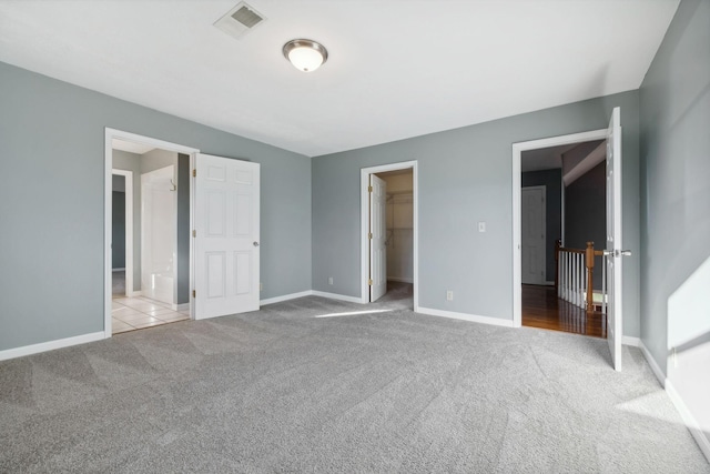 unfurnished bedroom featuring a spacious closet, a closet, and light carpet