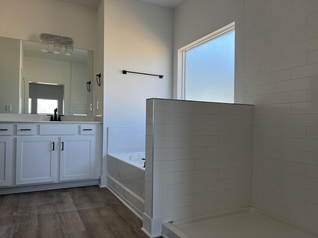 bathroom featuring a bath, tiled shower, wood finished floors, and vanity