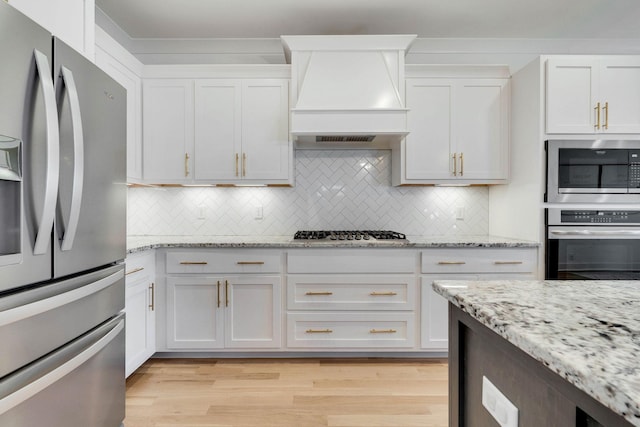 kitchen with decorative backsplash, appliances with stainless steel finishes, white cabinetry, and custom range hood