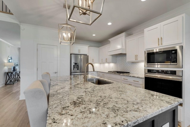 kitchen with stainless steel appliances, a kitchen island with sink, sink, decorative light fixtures, and white cabinets