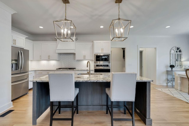 kitchen featuring white cabinets, pendant lighting, stainless steel appliances, and a kitchen island with sink