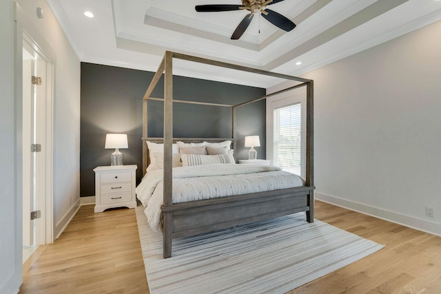 bedroom with a tray ceiling, ceiling fan, crown molding, and light wood-type flooring