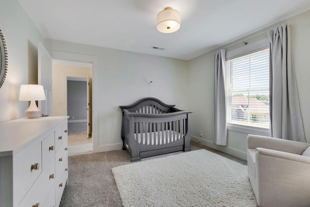 bedroom with multiple windows, light colored carpet, and a nursery area