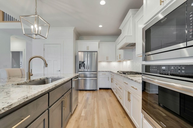 kitchen featuring sink, hanging light fixtures, stainless steel appliances, a notable chandelier, and white cabinets