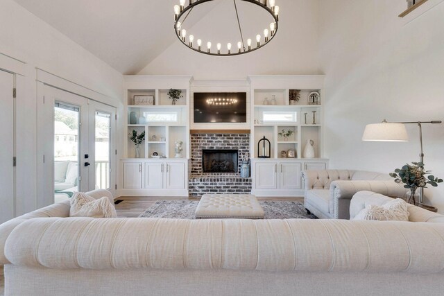 living room with french doors, light hardwood / wood-style flooring, a chandelier, lofted ceiling, and a fireplace