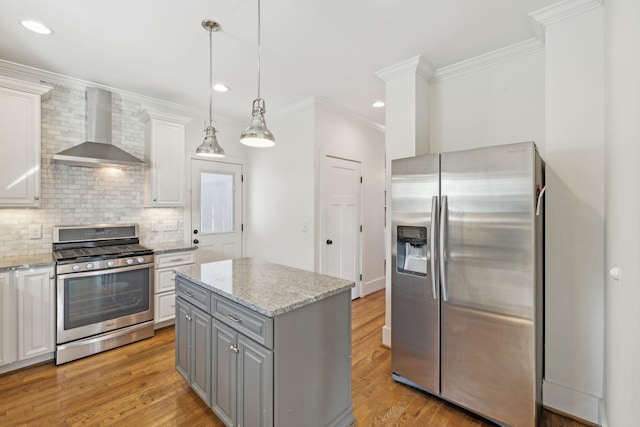 kitchen with light stone countertops, hanging light fixtures, stainless steel appliances, and wall chimney range hood