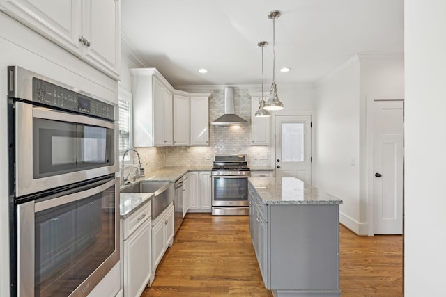 kitchen featuring appliances with stainless steel finishes, white cabinetry, a kitchen island, and wall chimney exhaust hood