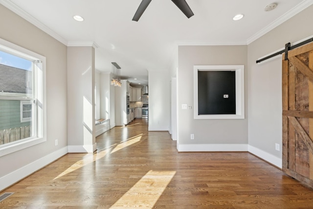 unfurnished living room with hardwood / wood-style floors, a barn door, ceiling fan, and crown molding