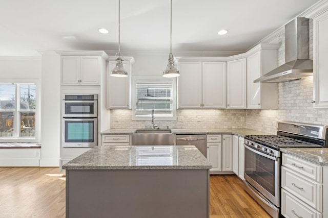 kitchen with wall chimney exhaust hood, stainless steel appliances, sink, pendant lighting, and white cabinets