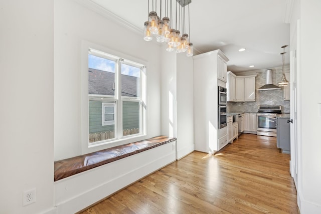 kitchen featuring backsplash, wall chimney exhaust hood, decorative light fixtures, stainless steel range oven, and white cabinets