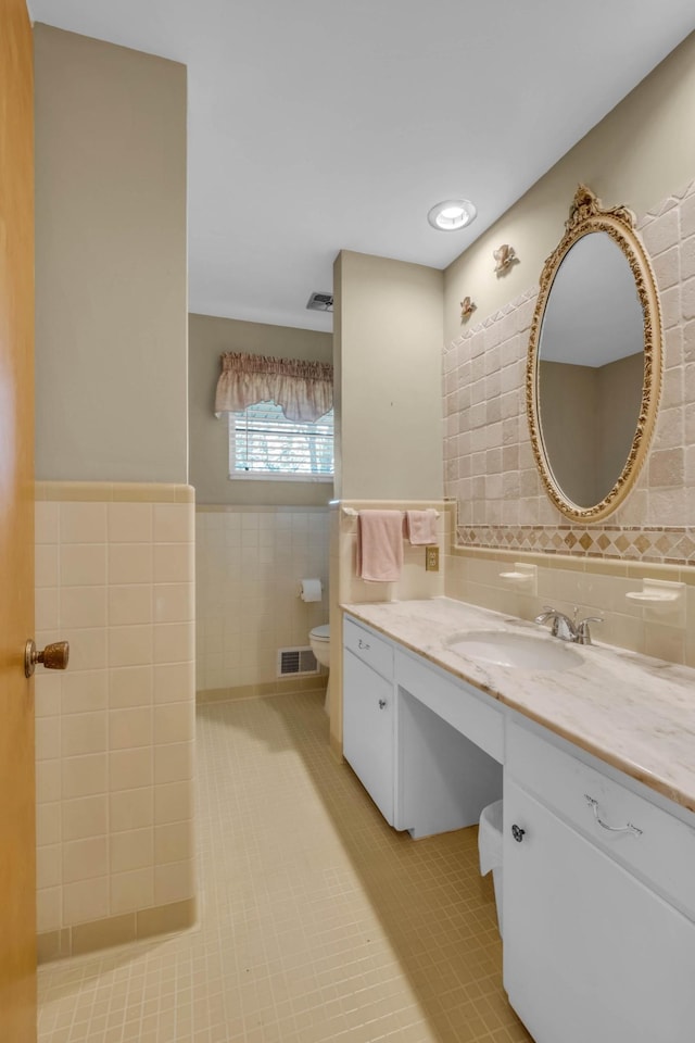 bathroom with tile walls, vanity, toilet, and tile patterned floors