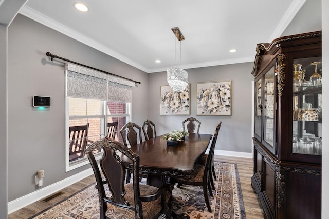 dining area featuring wood-type flooring, ornamental molding, and a notable chandelier