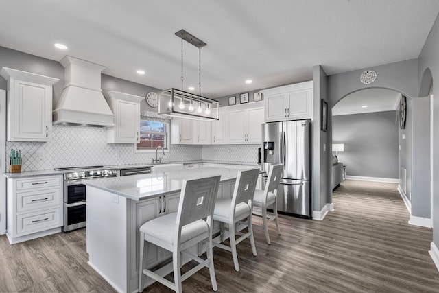 kitchen featuring light stone countertops, custom exhaust hood, stainless steel appliances, white cabinets, and a center island