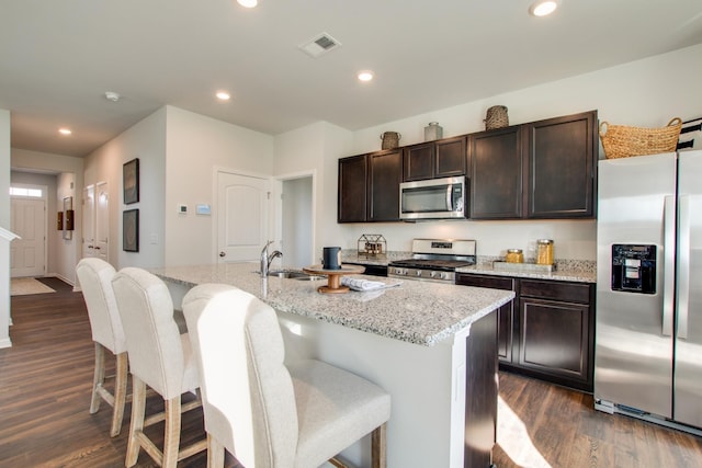 kitchen featuring dark wood-type flooring, a center island with sink, sink, light stone countertops, and stainless steel appliances