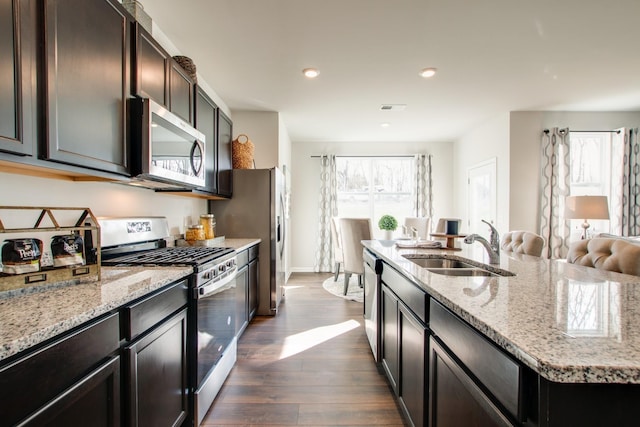 kitchen featuring sink, dark hardwood / wood-style floors, light stone countertops, an island with sink, and stainless steel appliances