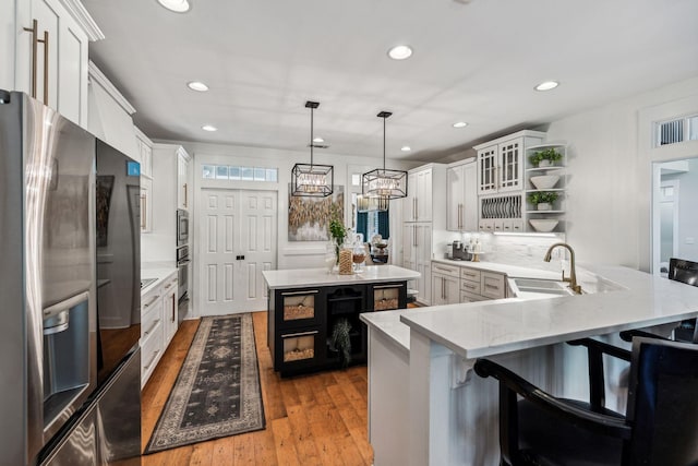 kitchen featuring kitchen peninsula, white cabinets, stainless steel appliances, and decorative light fixtures