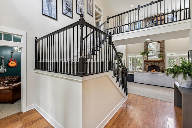 stairway with wood-type flooring, a towering ceiling, and a stone fireplace