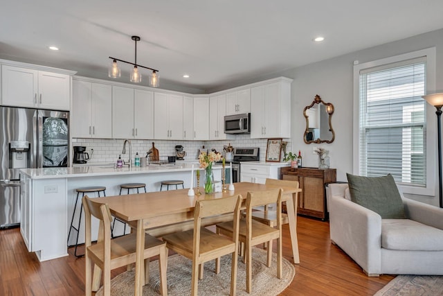 kitchen with decorative backsplash, appliances with stainless steel finishes, pendant lighting, white cabinets, and hardwood / wood-style floors