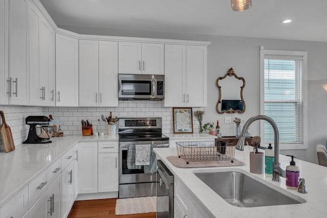 kitchen with backsplash, sink, light stone countertops, appliances with stainless steel finishes, and white cabinetry