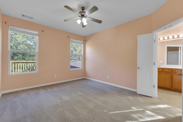 unfurnished bedroom with ceiling fan, light colored carpet, connected bathroom, and multiple windows