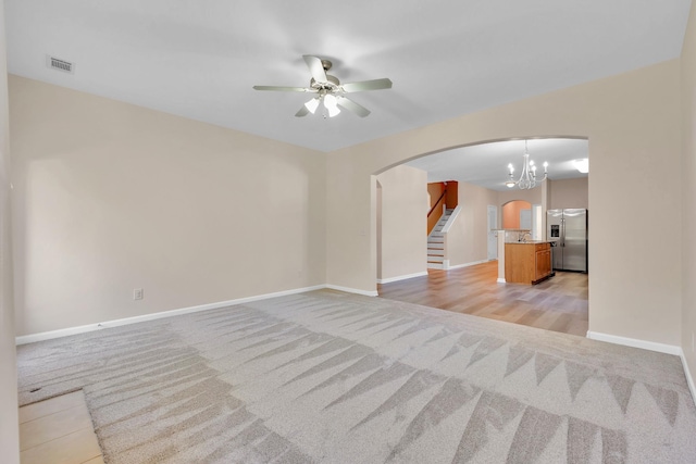 unfurnished living room featuring ceiling fan with notable chandelier and light colored carpet