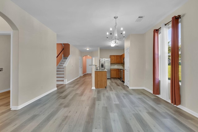 kitchen featuring appliances with stainless steel finishes, pendant lighting, light hardwood / wood-style flooring, a notable chandelier, and an island with sink