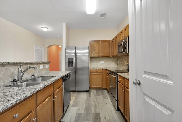 kitchen with light stone countertops, sink, light hardwood / wood-style flooring, decorative backsplash, and appliances with stainless steel finishes