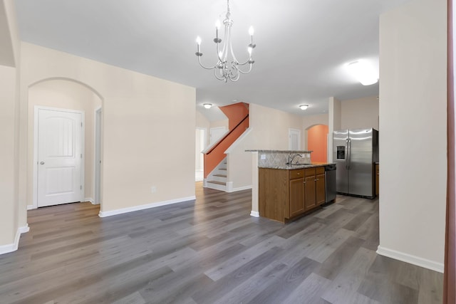 kitchen featuring pendant lighting, light wood-type flooring, an island with sink, a notable chandelier, and stainless steel appliances