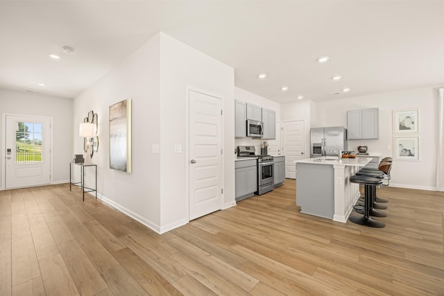 kitchen featuring a breakfast bar, a center island with sink, gray cabinets, appliances with stainless steel finishes, and light hardwood / wood-style floors