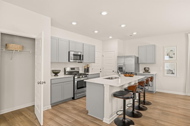 kitchen with a kitchen island with sink, a kitchen breakfast bar, sink, gray cabinets, and stainless steel appliances