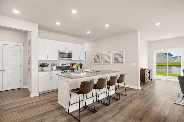 kitchen featuring a center island with sink, sink, light hardwood / wood-style floors, white cabinetry, and stainless steel appliances