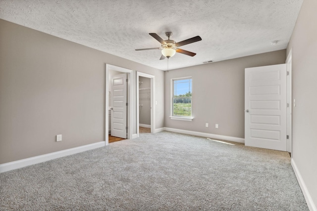 unfurnished bedroom with a spacious closet, ceiling fan, a closet, light colored carpet, and a textured ceiling