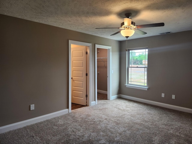 unfurnished bedroom featuring a spacious closet, ceiling fan, carpet, a closet, and a textured ceiling