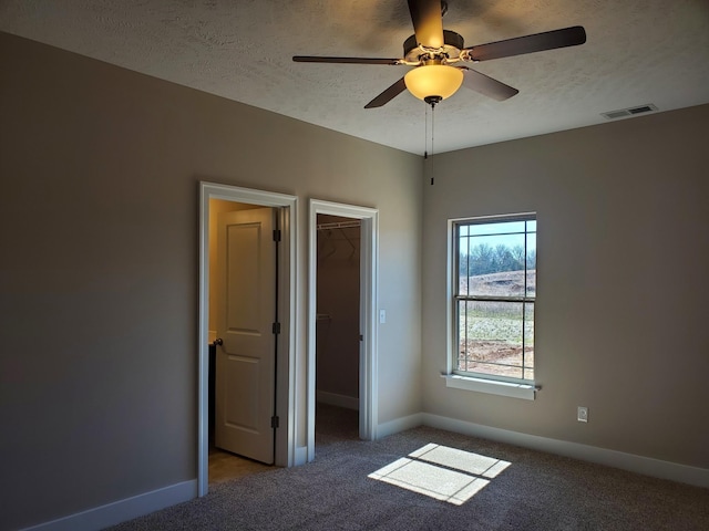 unfurnished bedroom featuring ceiling fan, carpet floors, a closet, a textured ceiling, and a walk in closet