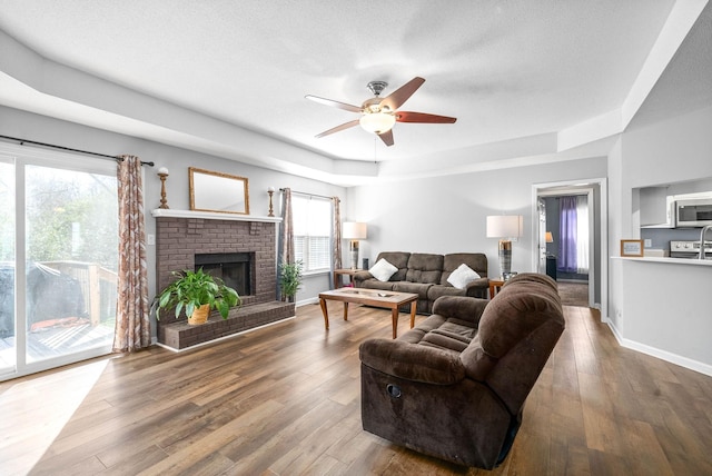 living room featuring a textured ceiling, a tray ceiling, ceiling fan, hardwood / wood-style flooring, and a fireplace