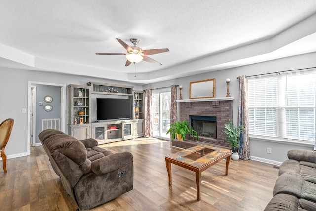 living room featuring a raised ceiling, a brick fireplace, ceiling fan, and a healthy amount of sunlight