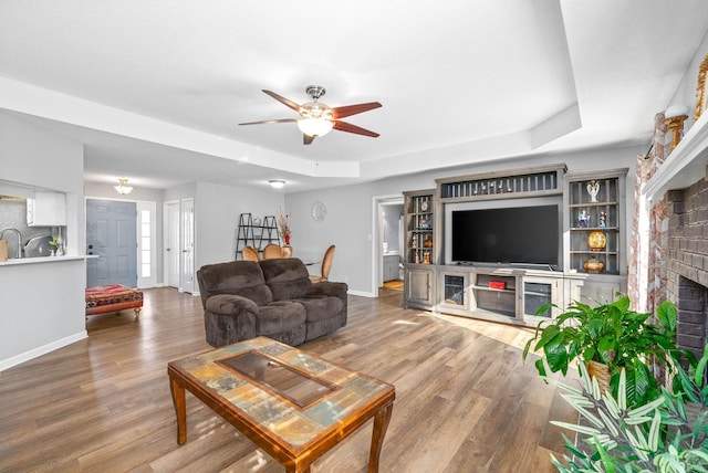 living room featuring a fireplace, hardwood / wood-style floors, a tray ceiling, and ceiling fan