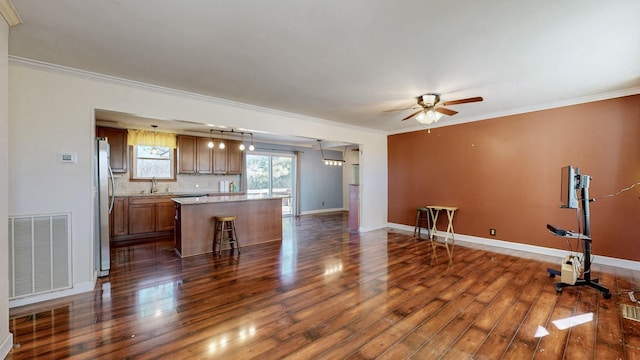 unfurnished living room with dark wood-style floors, visible vents, crown molding, and a sink