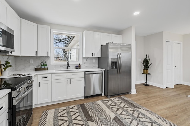 kitchen featuring sink, light hardwood / wood-style floors, decorative backsplash, white cabinets, and appliances with stainless steel finishes