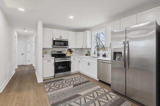 kitchen with sink, light wood-type flooring, tasteful backsplash, white cabinetry, and stainless steel appliances