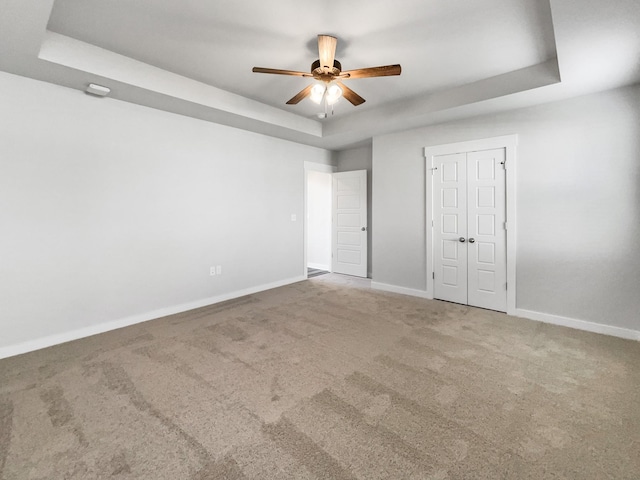 unfurnished bedroom with a raised ceiling, ceiling fan, a closet, and carpet floors