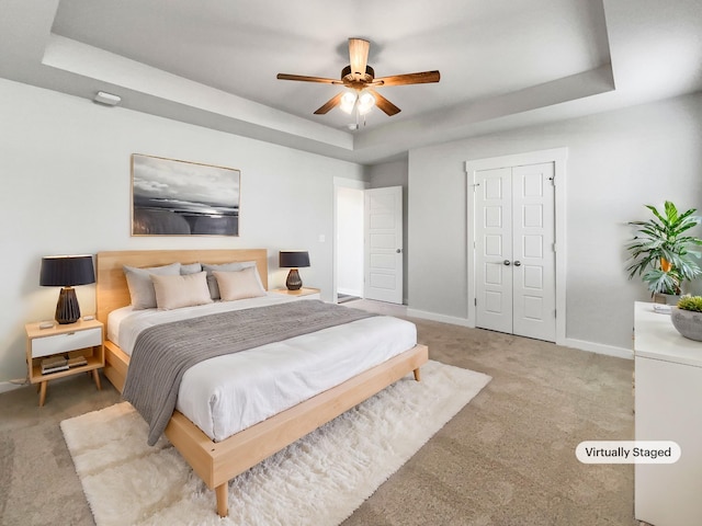 bedroom with light carpet, a closet, a tray ceiling, and ceiling fan