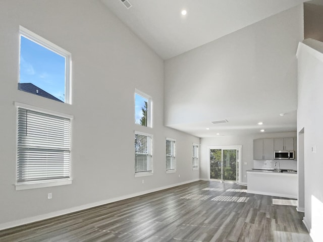 unfurnished living room featuring light wood-type flooring, high vaulted ceiling, and sink