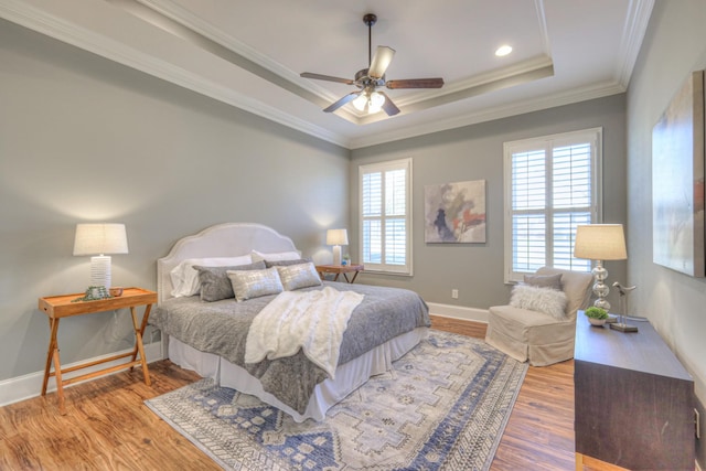 bedroom with a tray ceiling, ceiling fan, wood-type flooring, and ornamental molding