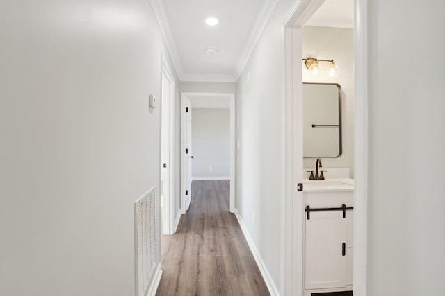 corridor with crown molding, sink, and light wood-type flooring