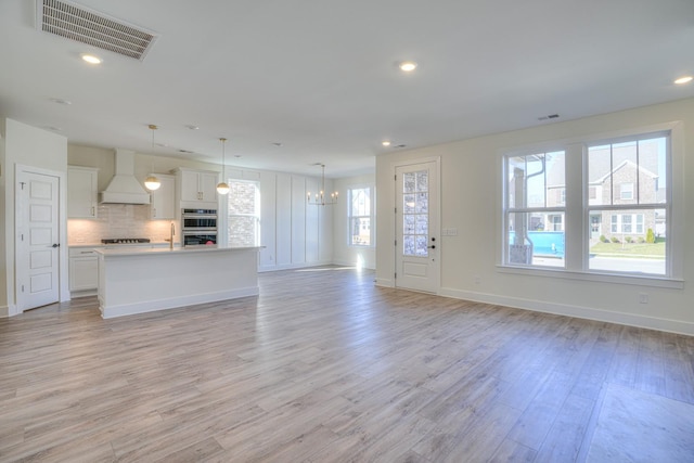 unfurnished living room with a notable chandelier, plenty of natural light, light wood-type flooring, and sink