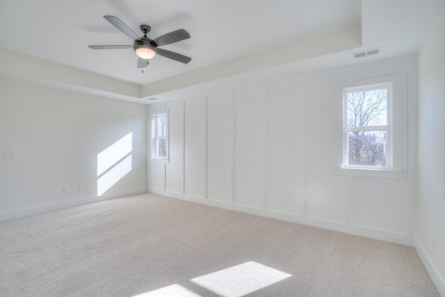 carpeted empty room with a raised ceiling, a wealth of natural light, and ceiling fan